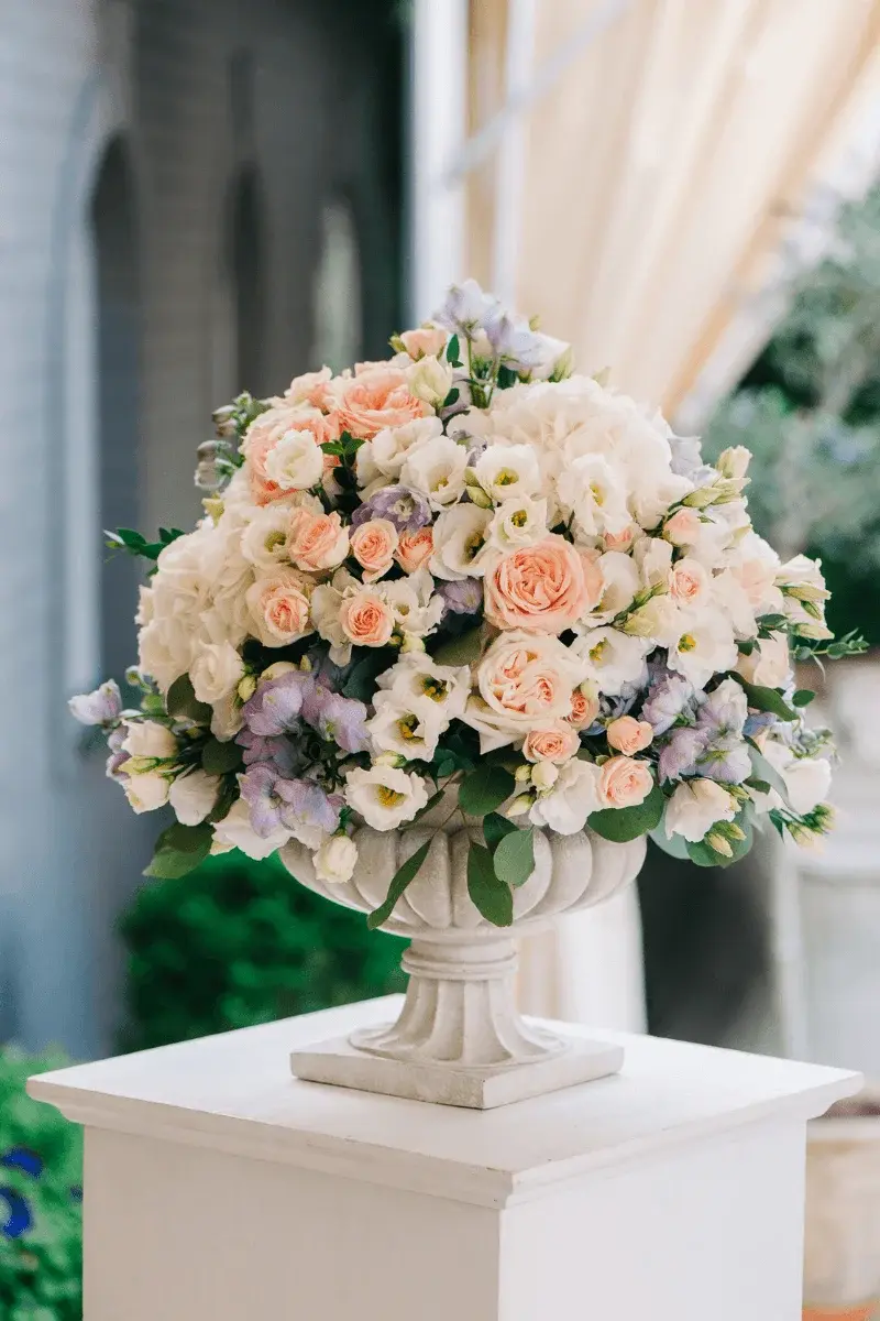 Seasonal floral centrepiece with peonies and foliage in a stone vase
